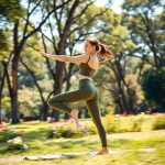 A woman in Olive Green hilary yoga pants performing a yoga pose in an Australian park.